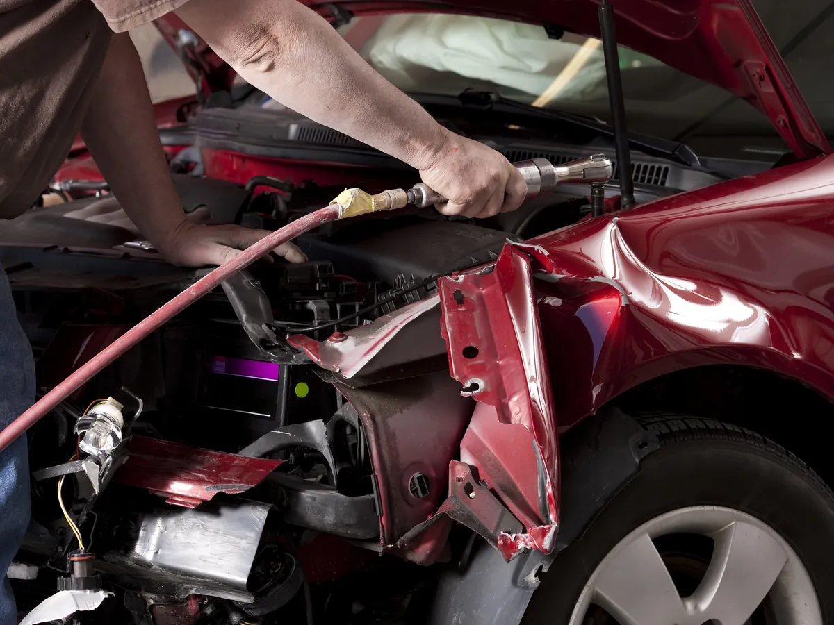 Technician repairing a damaged front bumper panel in a collision repair bay