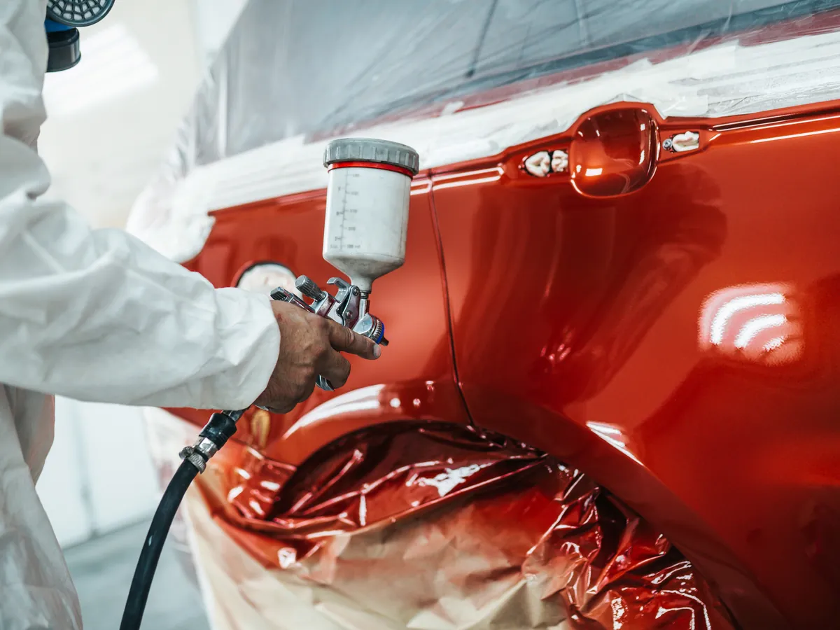 Technician applying automotive paint to a vehicle panel inside a paint booth