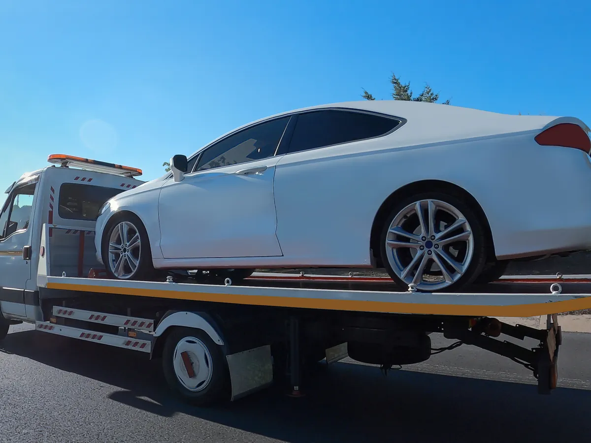 White sedan loaded on a flatbed tow truck on the road
