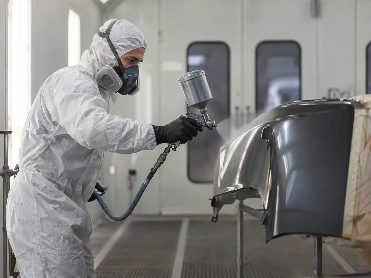 Technician applying automotive paint to a vehicle panel inside a paint booth