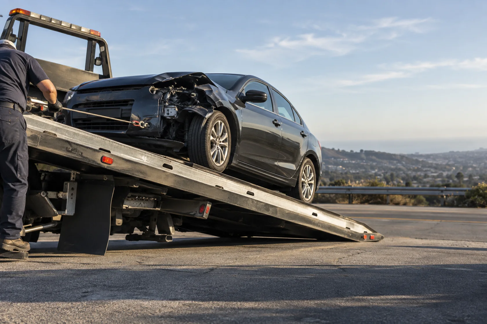 Damaged sedan being winched safely onto an unbranded flatbed tow truck